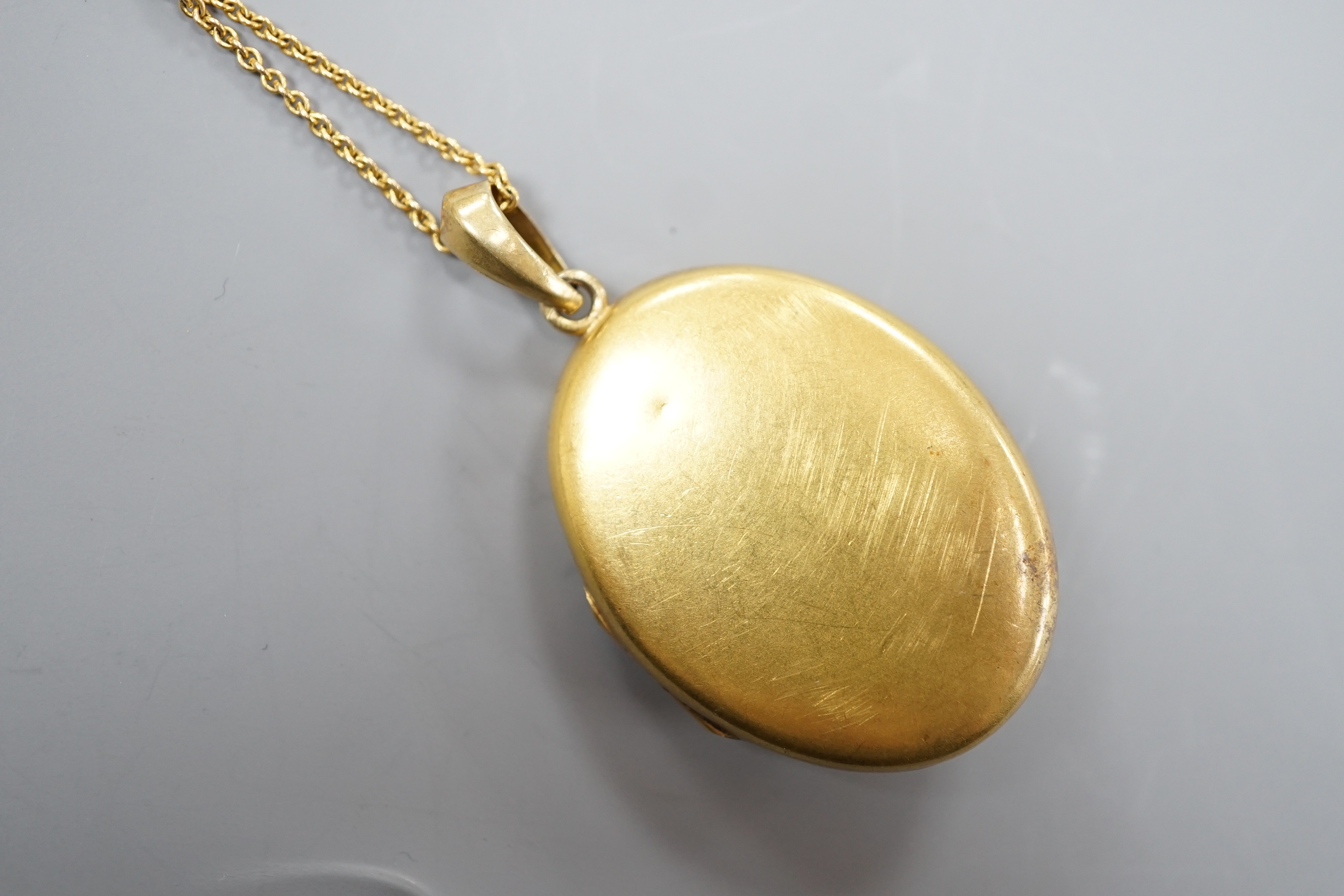 A yellow metal and seed pearl set oval locket stamped 56? (one flower motif with pearl missing), 39mm, on a fine link yellow metal chain, stamped ?ct